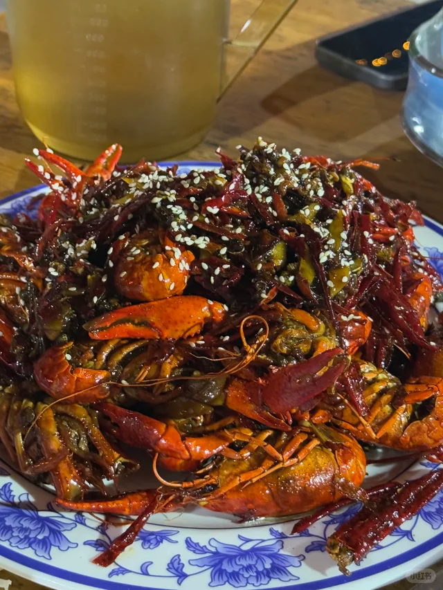 夜晚热闹的街边大排档,多张圆桌上摆满红色油亮的小龙虾,食客们戴着一次性手套开心地剥虾,背景有霓虹灯和烧烤烟雾,充满烟火气息 小龙虾夜市大排档场景