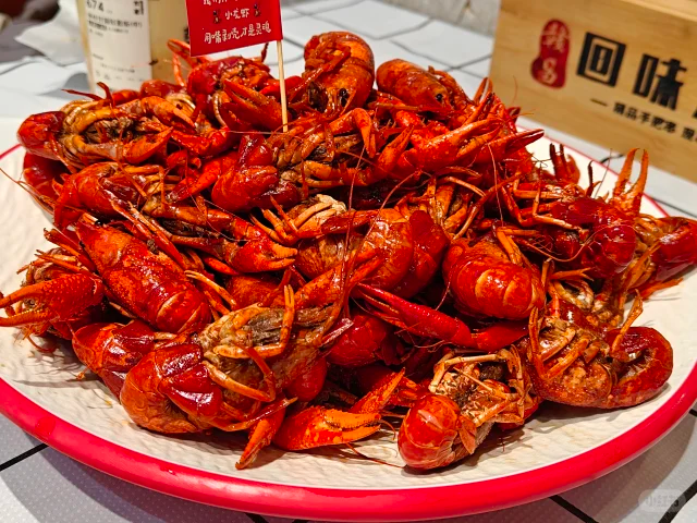 热闹的夏夜大排档,桌上摆着几盆红亮诱人的小龙虾,食客们戴着手套开心剥虾,啤酒杯旁堆满虾壳,背景灯光温暖,充满烟火气息和社交氛围,体现小龙虾作为社交美食的魅力 夜市小龙虾用餐场景