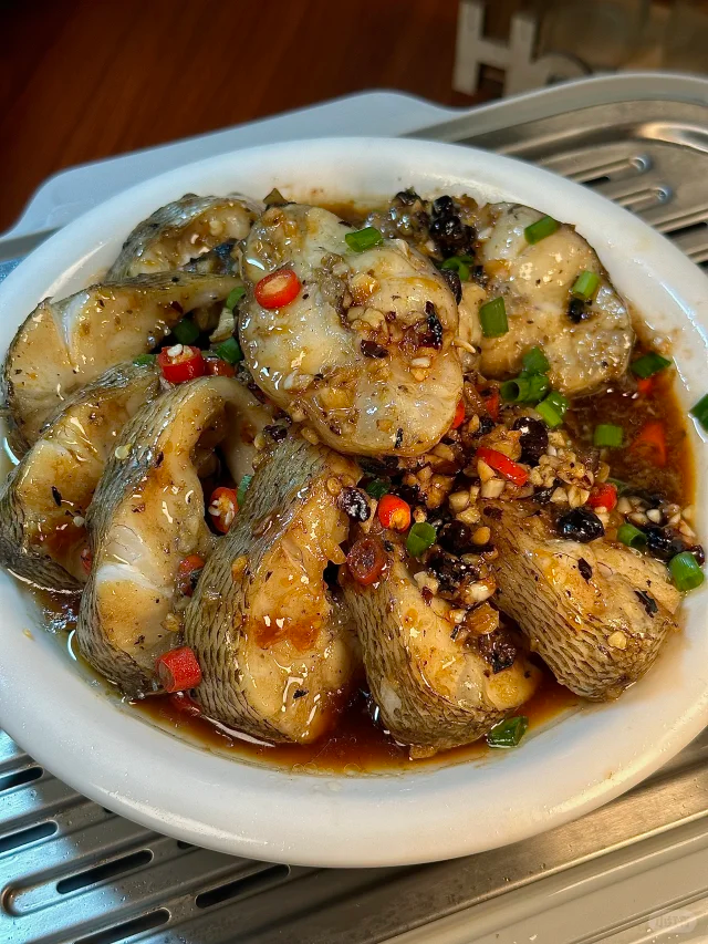 高清美食摄影:花椒薏米蒸鲫鱼成品摆盘,突出食材原色与蒸制工艺保留的湿润质感,体现药食同源家常化应用 花椒薏米蒸鲫鱼成品图:清蒸鲫鱼卧于青瓷盘中,鱼腹微张露出淡黄色炒薏米颗粒与青褐色花椒粒,表面淋少量姜葱油汁,盘沿点缀两片鲜紫苏叶,背景为木质餐桌与竹制蒸笼