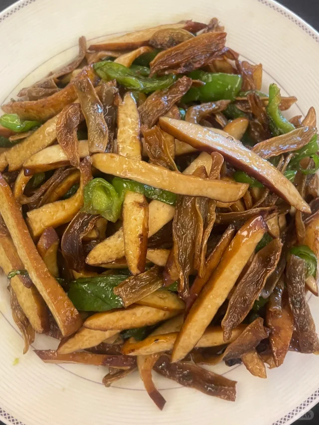 豆腐干条与青红椒条在炒锅中翻炒，酱汁微微收浓，整体色泽红润有光泽