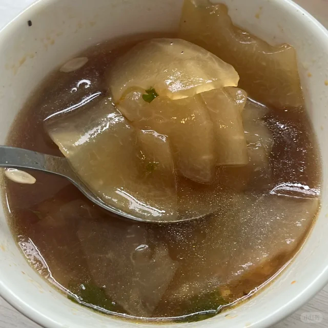 浅色陶瓷碗中盛放约半碗炒熟的冬瓜籽,籽粒呈均匀的浅金黄色,表面略有光泽,大小约为8×5毫米,形状扁平椭圆,背景为木质餐桌,旁边有一把金属小勺 炒熟的冬瓜籽盛放在陶瓷小碗中,呈金黄色,颗粒饱满