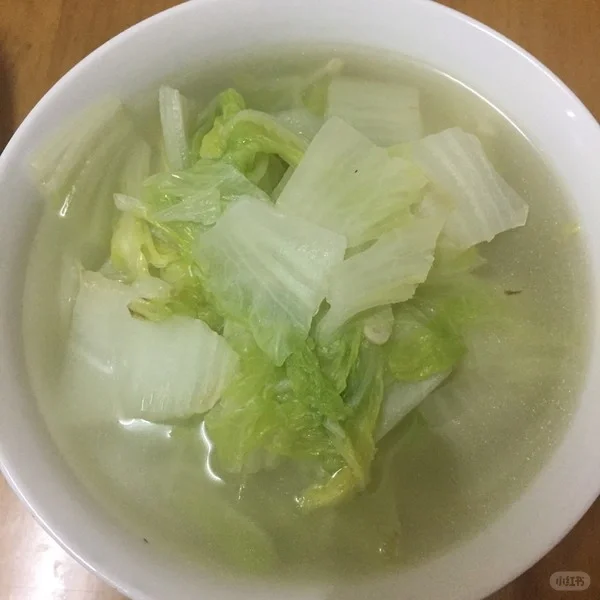 高清微距摄影展示白菜白萝卜清汤成品:汤体澄澈呈淡琥珀色,可见完整白菜叶脉纹理与白萝卜半透明环状结构,无油脂反光,汤面平静无浮沫,碗侧温度计清晰显示68℃,体现‘温而不烫、清而不寡’的药食同源汤品特质 特写镜头:透明玻璃碗中盛放温热白菜白萝卜清汤,汤色浅琥珀透亮,漂浮数片嫩黄白菜叶与半透明萝卜片,汤面无油星,碗旁放置不锈钢勺与温度计显示68℃