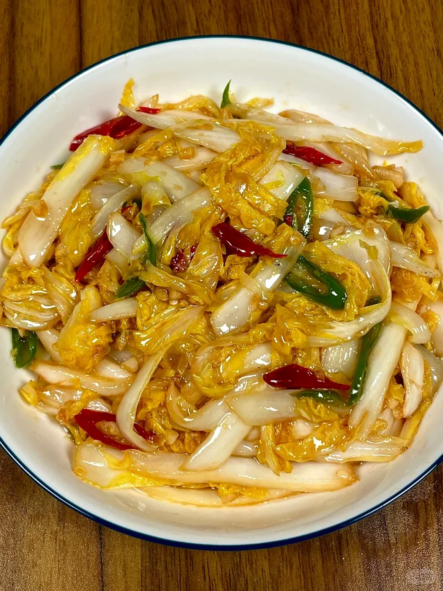 厨房烹饪场景：不锈钢锅中娃娃菜段正在清炒，菜叶微卷、色泽碧绿透亮，锅边点缀蒜末与枸杞，升腾热气，展现‘娃娃菜’家常做法的清爽质感