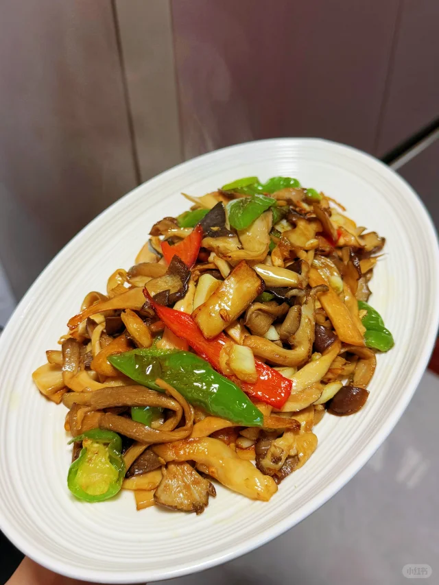 家庭烹饪场景:大蒜青椒炒平菇过程实拍,展示平菇在中式快炒中的应用方式 家庭厨房中正在用铁锅翻炒平菇的场景,锅中平菇与大蒜、青椒混合,热气腾腾,旁边摆放洗净的鲜平菇原料