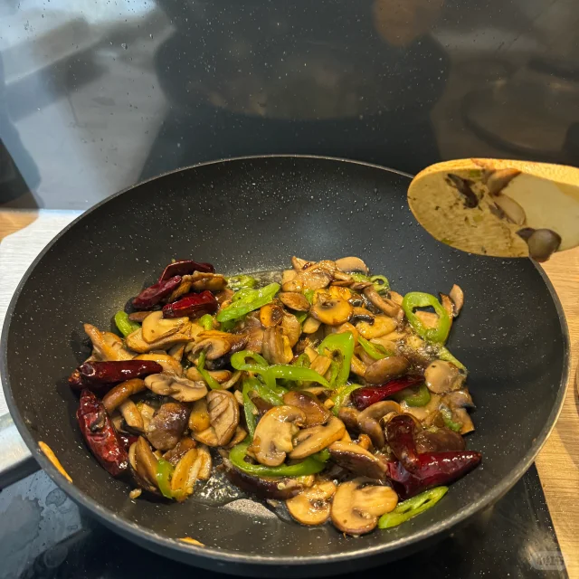 高清俯拍:盘中蒜薹炒蘑菇色泽分明,蒜薹段长度均匀、无焦边,口蘑片完整微卷、边缘略带琥珀色焦边,整体油光自然不浮腻,背景为原木砧板与竹筷,凸显农家时令感 成品特写:青翠蒜薹段与奶白口蘑片交错铺陈于浅色瓷盘中,表面油润透亮无水渍,撒有细碎红椒丝点缀,热气隐约可见