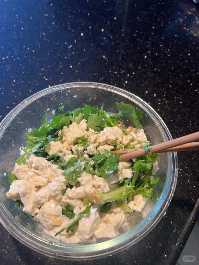 中式凉拌香菜配菜场景：翠绿香菜段与嫩豆腐丁、芝麻、少许蒜末混合，淋浅色香油，盛于青瓷小碗中，体现家常健康食用方式