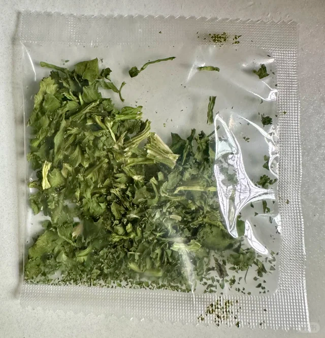 一张整洁的白色桌面上摆放着多种香菜深加工产品,包括玻璃瓶装香菜油、密封袋装香菜粉、脱水香菜干、真空包装鲜香菜段,旁边配有标签说明和营养成分表,背景虚化呈现现代食品加工厂环境 香菜深加工产品展示图