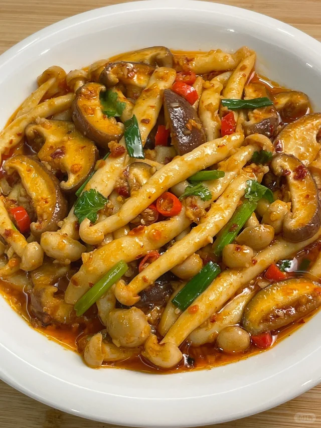 一盘刚出锅的清炒双菇菜肴特写,盘中混合着灰白色的鲜平菇片与浅黄色的金针菇丝,表面泛着油光并点缀几粒蒜末,部分边缘微焦呈金黄色,整体呈现湿润而不积水的状态,背景虚化的灶台上可见炒锅与调味瓶,营造出家庭烹饪的真实氛围 平菇与金针菇合炒出锅成品图