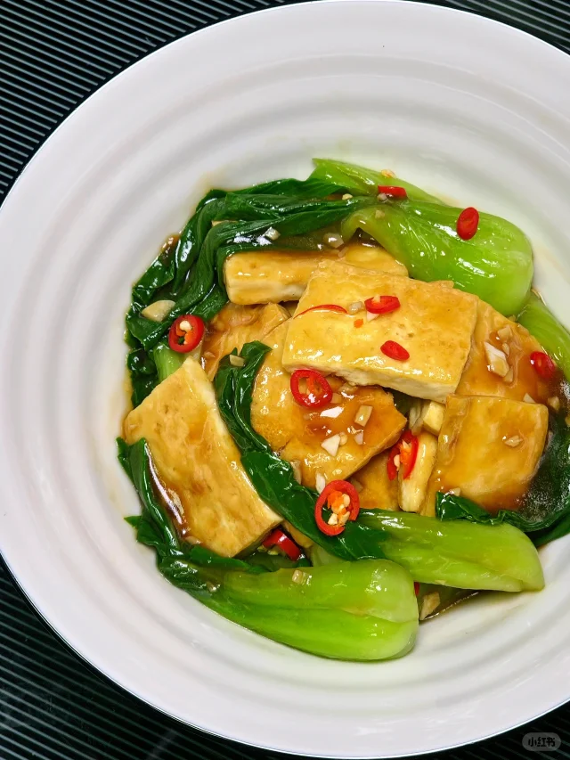 一盘刚出锅的娃娃菜炒豆腐，豆腐呈金黄色，娃娃菜翠绿，表面有光泽的酱汁覆盖