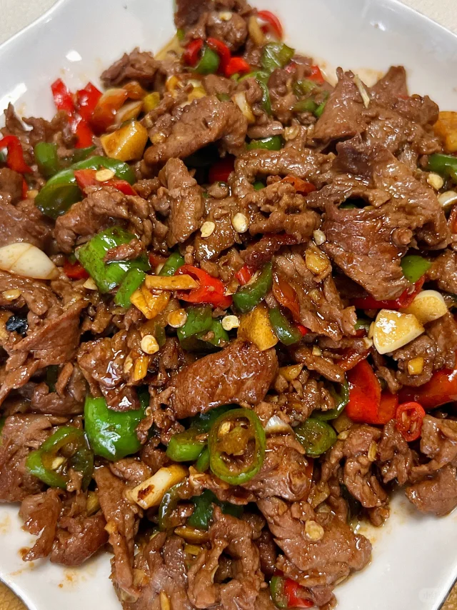 高清俯拍:成品泡椒牛肉呈现诱人油亮色泽,牛肉片厚薄均匀、边缘微卷,泡椒碎分布自然,酱汁浓稠挂片不流散,体现精准火候控制 泡椒牛肉出锅特写:深红油亮的泡椒粒与翠绿小米辣点缀在嫩粉色牛肉片上,肉片完整舒展无碎屑,表面裹着晶莹酱汁,盘底无多余汤水