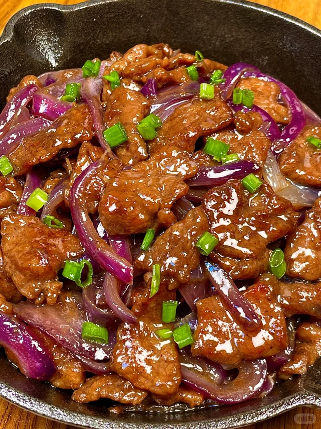 红烧牛肉洋葱版完成状态高清图:牛肉块形完整酥软、煸洋葱丝金黄透亮、酱汁浓稠油亮挂勺,体现‘酥而不柴、甜香平衡’的核心品质 红烧牛肉成品特写:深红油亮牛肉块堆叠,半透明煸炒洋葱丝缠绕其间,表面点缀翠绿葱花,酱汁浓稠挂勺呈琥珀色,背景为青花瓷炖锅