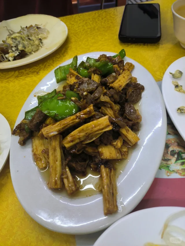 白色瓷盘中盛放刚出锅的松花菜炒牛肉,乳白色花菜与深褐色牛肉分明可见,点缀绿色葱段与红色辣椒圈;背景虚化的木质餐桌衬托温馨家庭用餐氛围,右下角有一碗米饭呼应主食搭配 成品摆盘特写