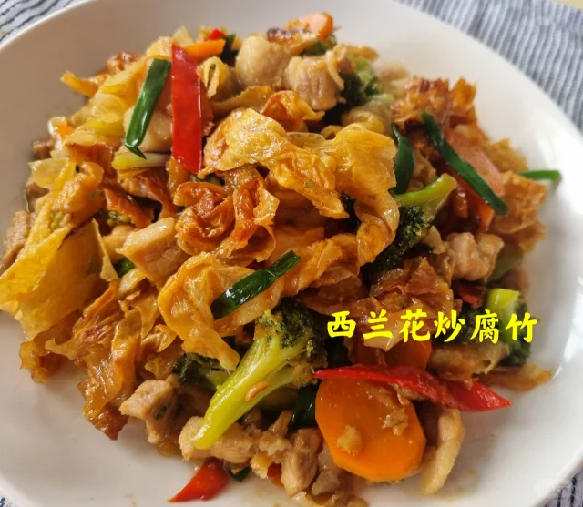 新鲜西兰花呈深绿色,花球紧密,茎部洁白脆嫩;干制腐竹为金黄色条状,表面有自然油亮光泽,两者并列摆放于木质砧板上,背景为厨房环境 腐竹与西兰花原材料特写