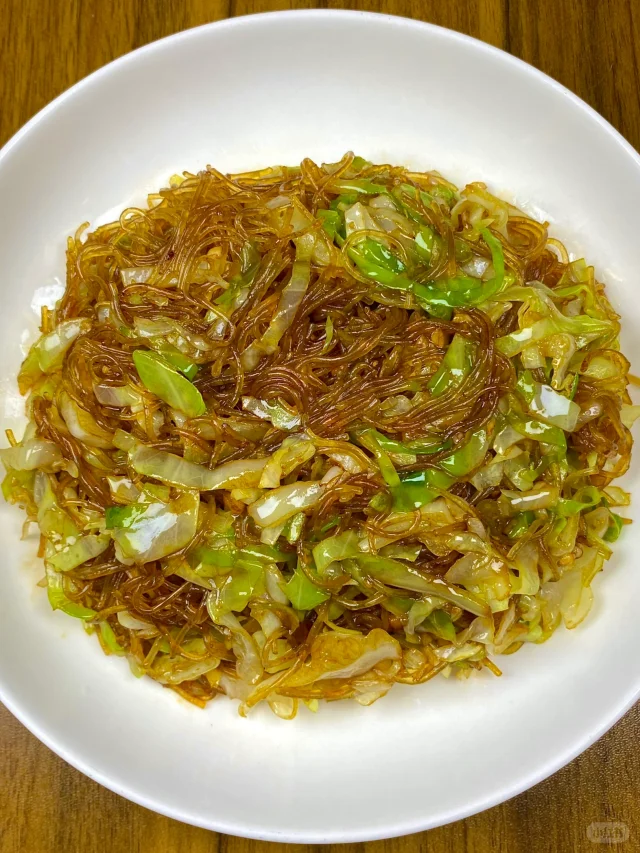 厨房场景：不锈钢炒锅中正在翻炒的圆包菜丝，色泽鲜绿油亮，辅以蒜末、干辣椒与少许五花肉片，锅气升腾，灶台整洁，体现家常热炒的烟火气与圆包菜的实用烹饪属性