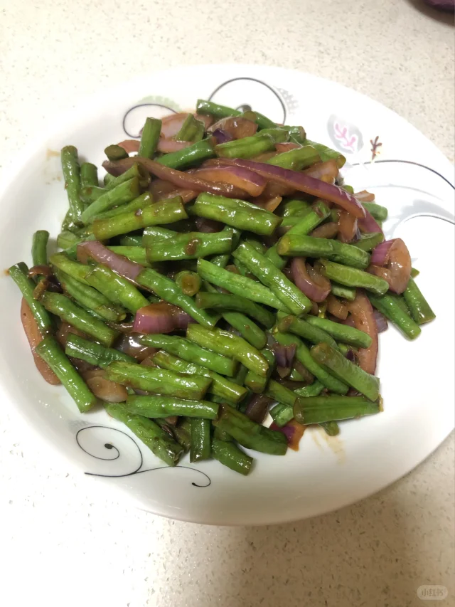 成品装盘特写：翠绿四季豆与半透明洋葱丝交织，油润亮泽，撒少量白芝麻，青瓷浅盘衬托