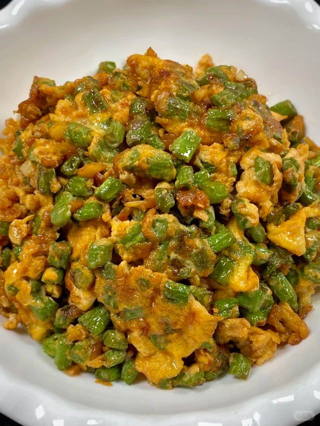 一盘刚出锅的白不老豆角炒鸡蛋,豆角呈翠绿色,鸡蛋为金黄色块状,二者交错分布,表面略有油光,撒有少量葱花点缀,盛放在白色瓷盘中,背景为家庭厨房灶台 白不老豆角炒鸡蛋成品图