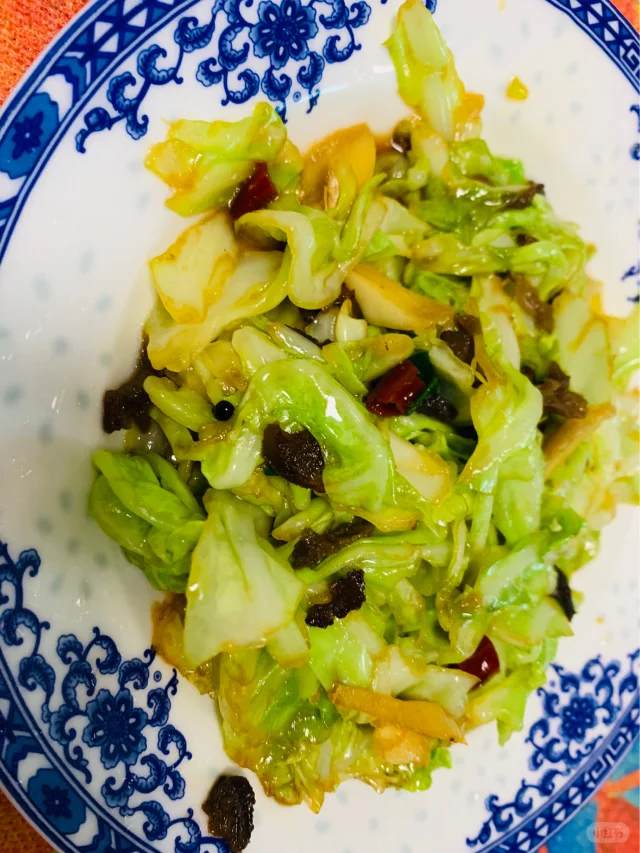 一盘刚出锅的清炒沙参叶,盛放在白色瓷盘中,叶片碧绿油亮,蒜片点缀其间,表面泛着淡淡油光,背景为木质餐桌,营造出温馨家常氛围 清炒沙参叶成品图