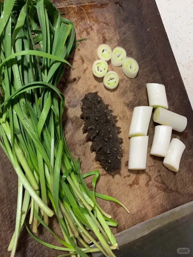 海参炒韭菜成品特写：青翠韭菜段缠绕琥珀色Q弹海参，点缀金黄蒜片与葱白，盘底有薄亮酱汁光泽，热气氤氲，呈现“干香油润、翠绿不蔫、海参挺括”的视觉效果