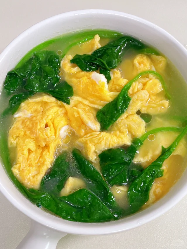 高清俯拍图:新鲜菠菜经焯水切碎后与蛋液充分混合蒸制而成的菠菜蒸蛋成品,呈现自然分层结构——上层为碧绿菠菜颗粒,下层为细腻金黄蛋羹,表面光滑湿润,无焦边或蜂窝状气孔,体现精准火候控制 菠菜蒸蛋成品特写:翠绿菠菜碎均匀嵌入嫩滑蛋羹表面,蛋液呈半透明琥珀色,无气孔塌陷,配白瓷浅碗与竹筷