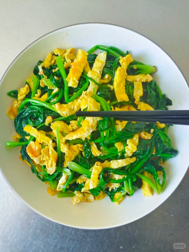 高清俯拍:菠菜炒蛋成品,菠菜翠绿挺括无萎蔫,蛋块呈湿润金黄色颗粒状,盘底干燥无水渍,撒5粒白芝麻点缀,体现‘嫩滑不水、翠绿不黄’核心卖点 菠菜炒蛋成品特写:青翠菠菜段与金黄蓬松蛋块交错铺满白瓷盘,表面泛自然油光,撒少许白芝麻,背景虚化木质餐桌