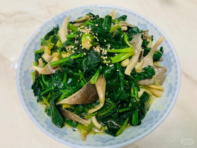 一盘刚出锅的清炒菠菜香菇菜肴，色泽翠绿与棕褐相间，表面略带油光，配有瓷盘和木筷