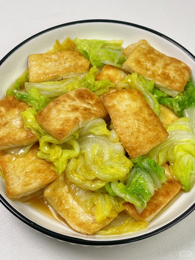 厨房中正在用锅煮娃娃菜的画面,锅内娃娃菜与白豆腐共煮,汤色清亮,旁边配有生姜片和葱段,体现温性食材搭配的健康烹饪方式 娃娃菜家庭烹饪场景